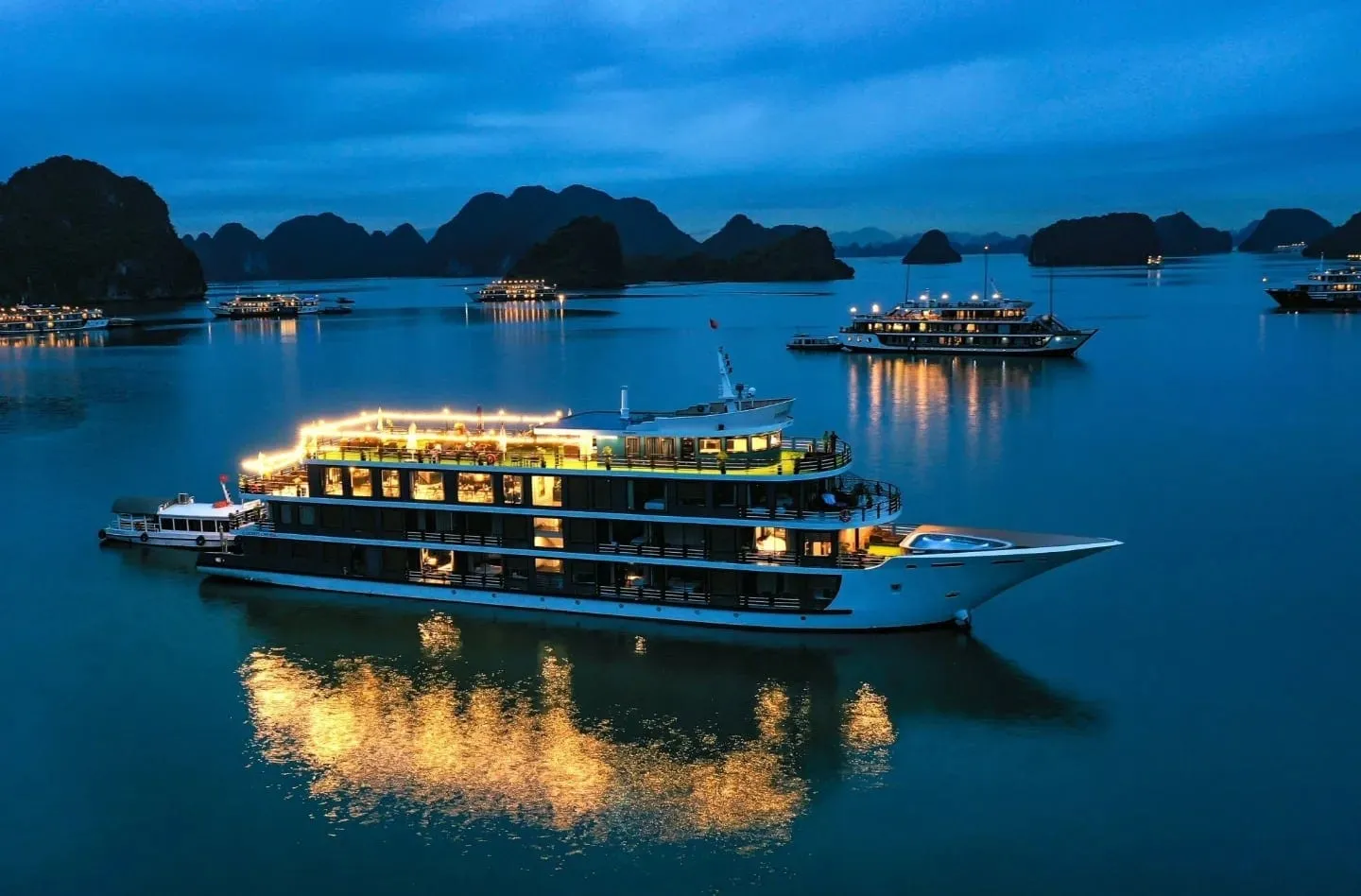Rosy Cruise lit up at night, every window gold and the light spilling across the water in a long reflection
