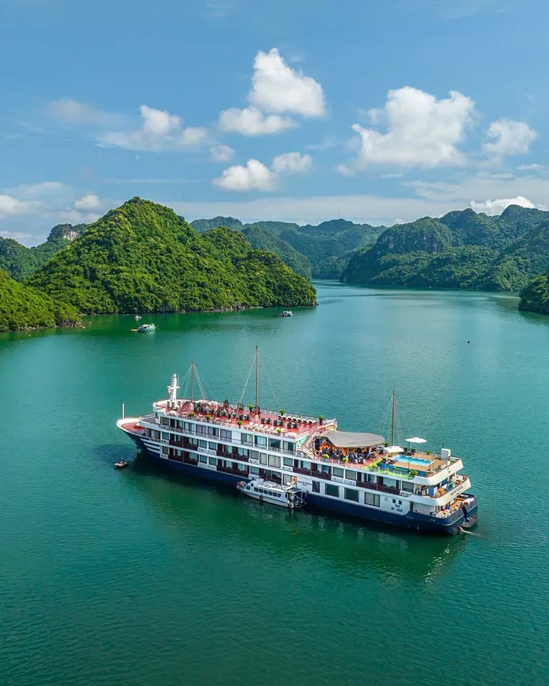 A multi-deck cruise ship with passengers on board floats in turquoise water surrounded by dramatic limestone karst islands.