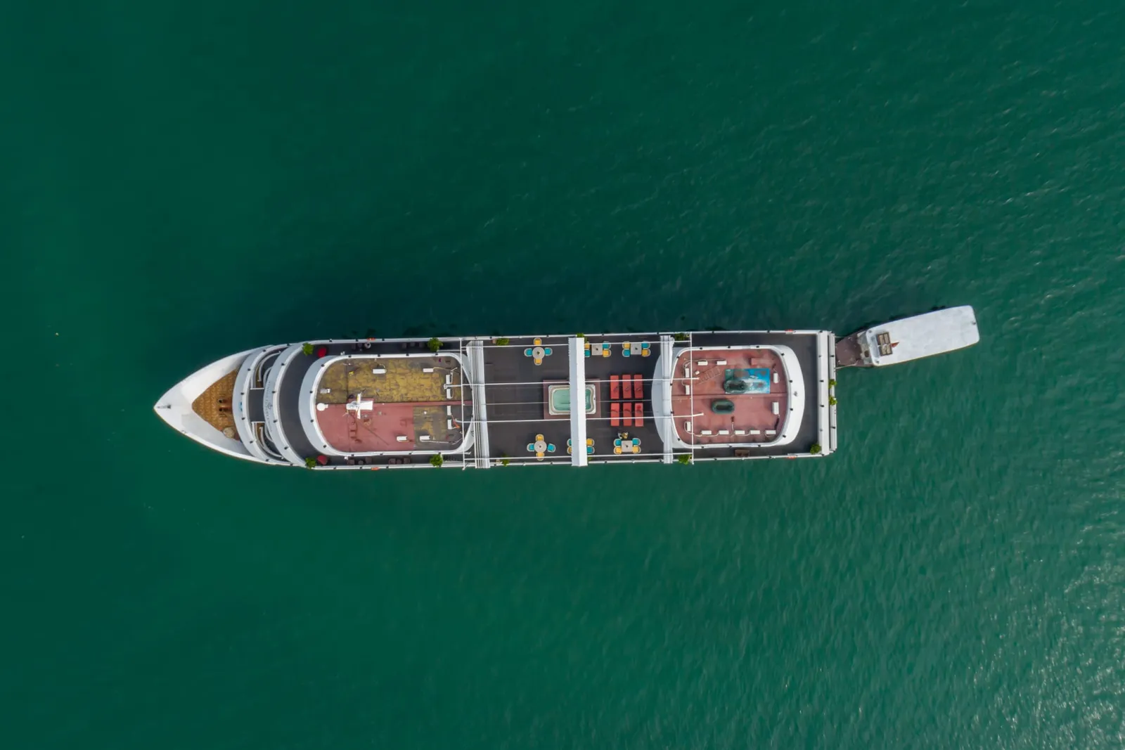 Aerial view of a white cruise boat with visible deck layouts floating on green-teal water.