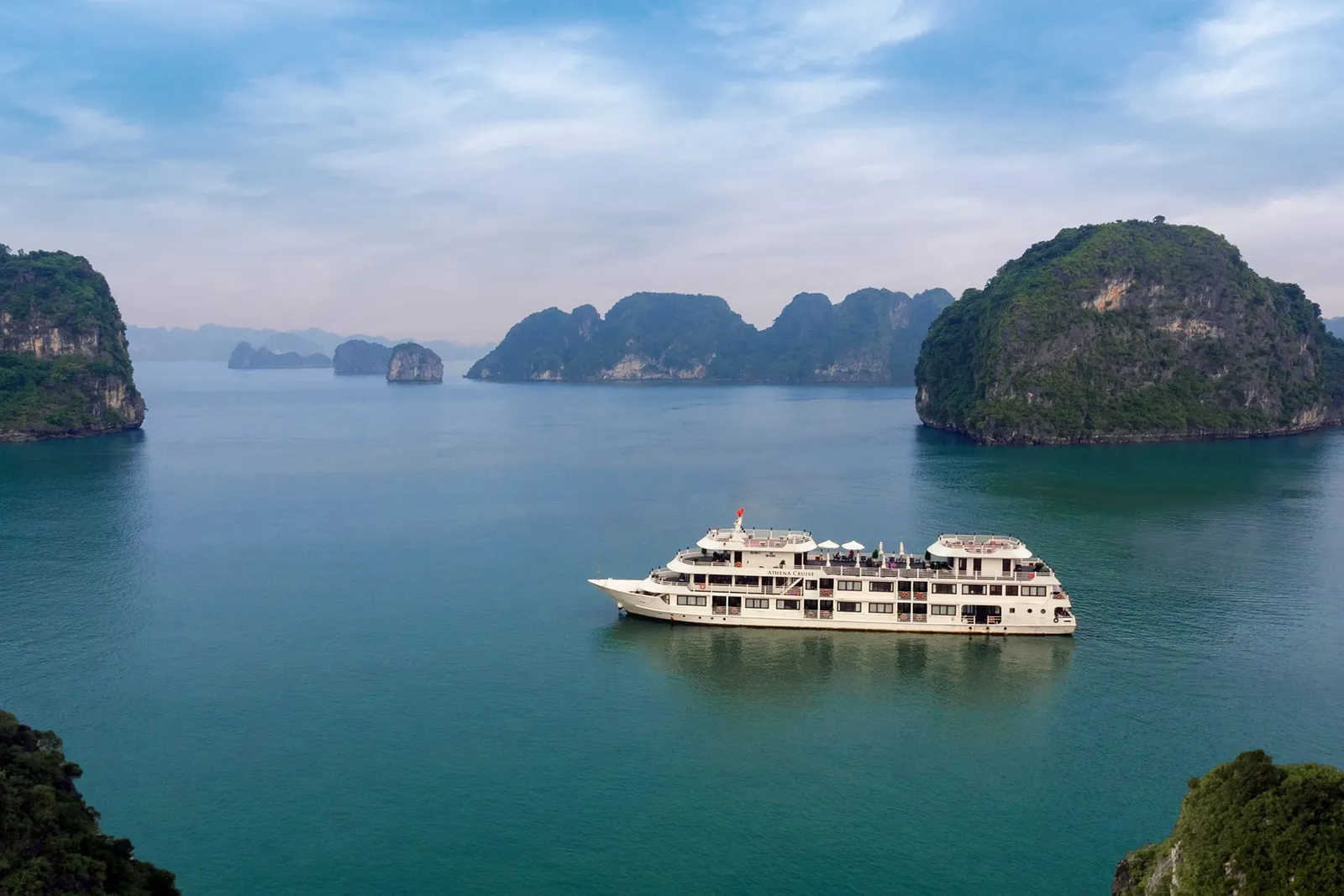 A white multi-deck cruise ship floats in calm turquoise water surrounded by dramatic limestone karst islands.
