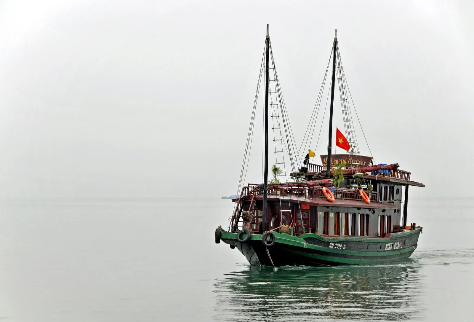 A two-masted wooden boat at anchor in misty water