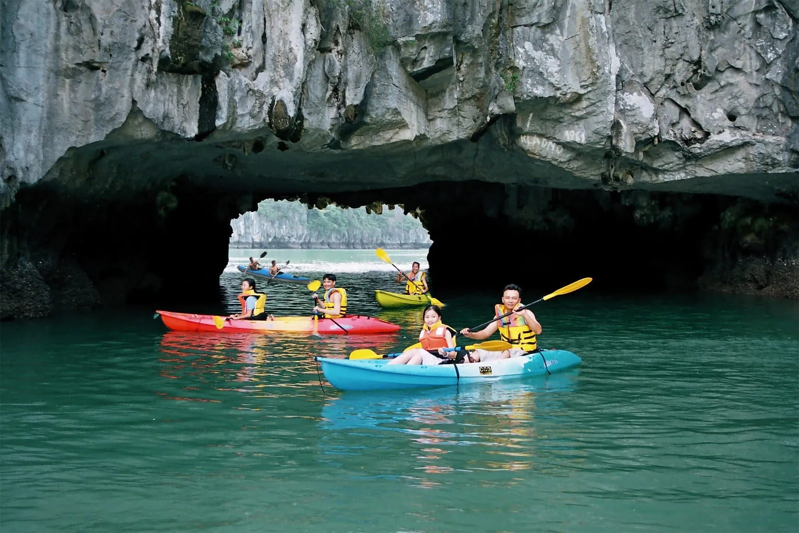 Kayakers paddling through a low rock arch into a sheltered lagoon