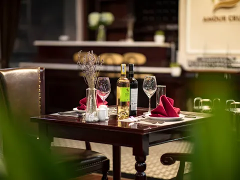 A set dining table with red napkins, wine bottles, glasses and a lavender vase in an indoor restaurant, with a wall sign reading 'Amour Cruise' in the background.