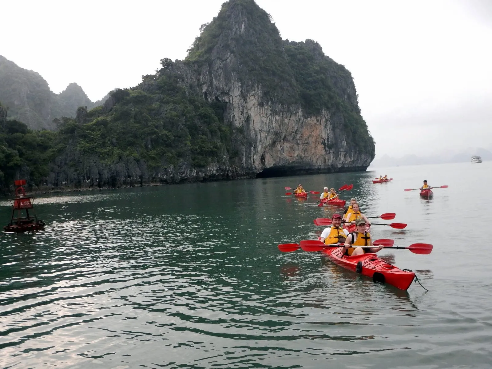 A group of kayaks on open water below a limestone island in Bai Tu Long Bay