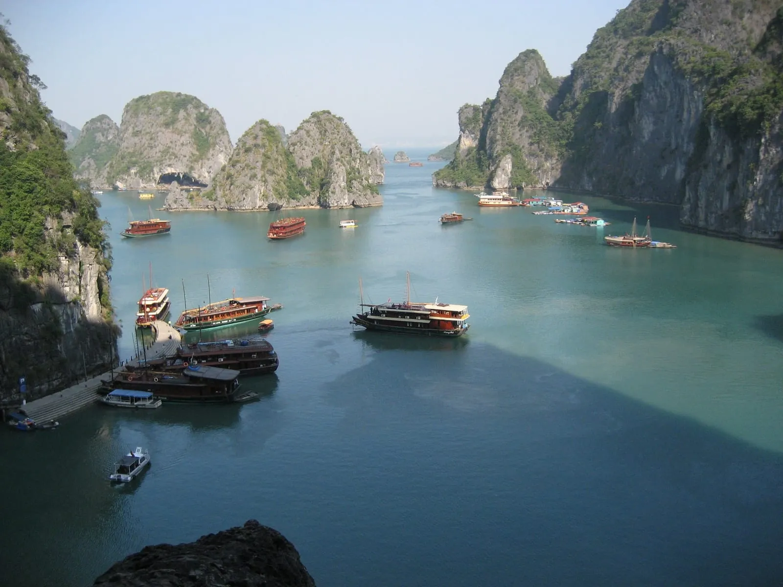Boats moored in a sheltered bay below limestone islands, seen from a cave entrance