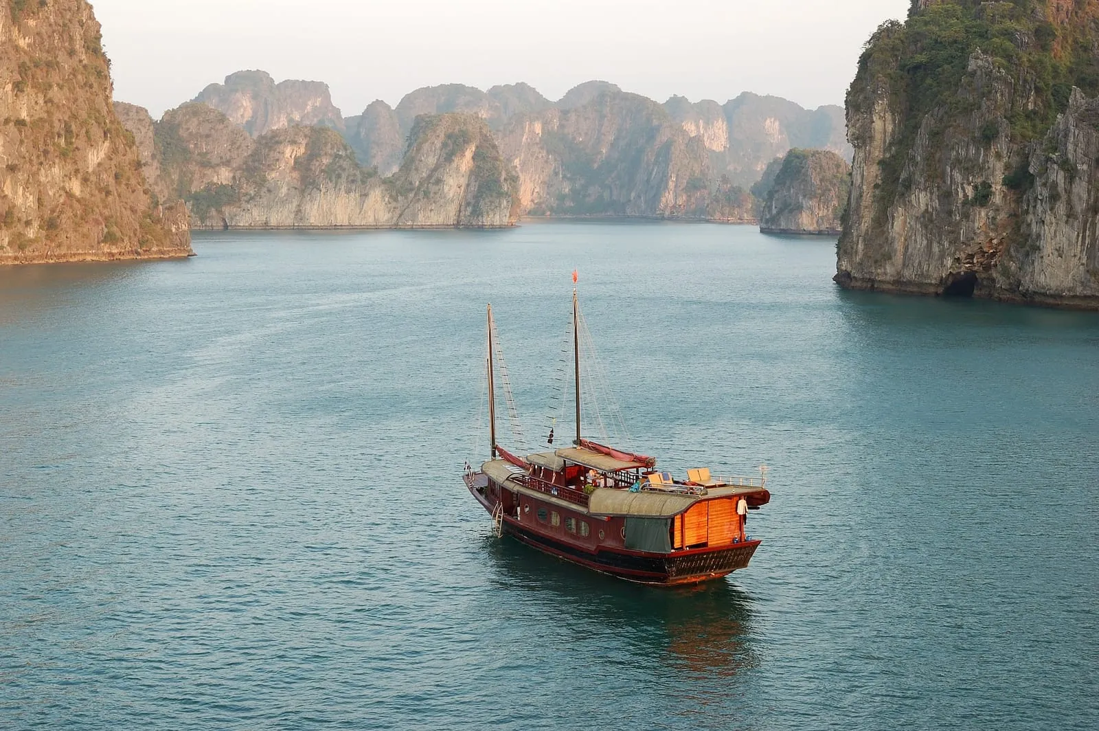 A wooden boat with two masts sailing past limestone cliffs